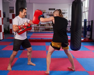 Koçla çocuk kickboxu eğitimi, spor salonunda pedlere vurmak.