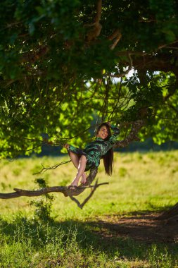 Genç İspanyol manken ormanda meşe ağaçlarıyla yeşil elbiseli.