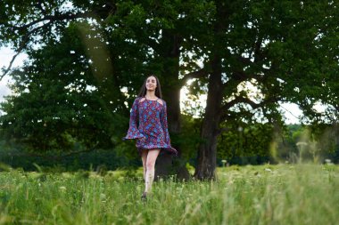 Çiçekli bir elbiseyle, çok yaşlı meşe ağaçları ve ormanlı bir çayırda poz veren genç ve güzel bir Latin manken. 