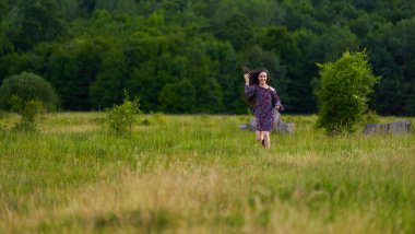 Çiçekli elbiseli çekici Latin model gündüz çayırda koşuyor. 