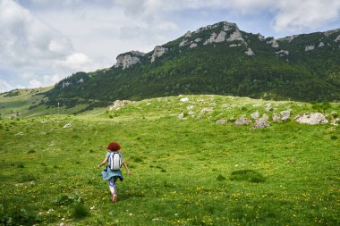 Yazın başında sırt çantalı kızıl saçlı bir kadın dağlarda tek başına yürüyüş yapıyor.