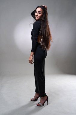 Gri stüdyo arka planında poz veren siyah elbiseli, uzun saçlı, güzel İspanyol bir kadın.