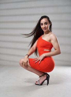 Güzel, atletik, kırmızı mini elbiseli, gri arka planda büyüleyici bir kadın.