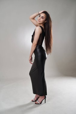 Gri arka planda poz veren siyah elbiseli, uzun saçlı, güzel esmer kadın.