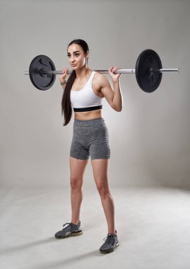 Atletik fitness kadını gri arka planda halter çömelmesi yapıyor.