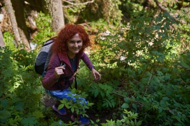 Sırt çantalı kızıl saçlı kadın güneşli yaz gününde dağlarda yürüyüş yapıyor.