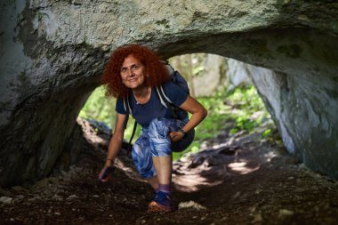 Sırt çantalı kızıl saçlı kadın güneşli yaz gününde dağlarda yürüyüş yapıyor.
