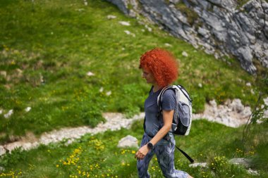Sırt çantalı kızıl saçlı kadın dağlarda yürüyüş yapıyor.