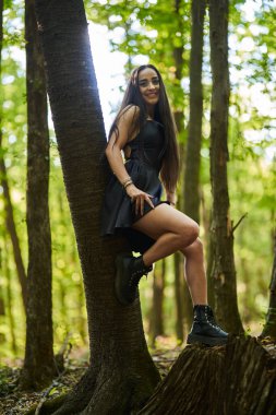 Ormanda poz veren mini siyah elbiseli güzel esmer kadın.