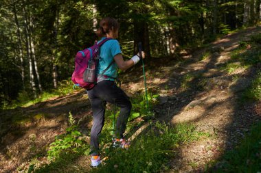 Yürüyüş direkleri olan kadın yürüyüşçü ormandaki patikalarda dağlara doğru yürüyor.