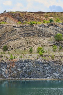 Bazalt, kumtaşı, yosun ve diğerleri gibi çeşitli kaya oluşumları terk edilmiş bir taş ocağında, gök mavisi gölün duvarlarını oluşturur.