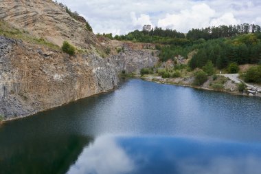 Terk edilmiş bazalt ve yeşil ormanlı kumtaşı ocaklarında oluşan gök mavisi göl manzarası.