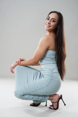 Açık mavi elbiseli çekici Latin kadın ve gri arka planda yüksek topuklu. 