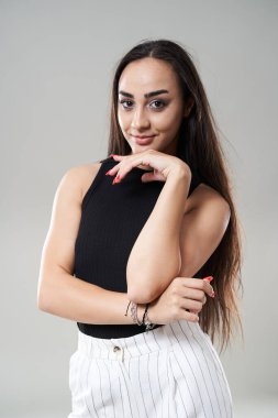 Beyaz pantolonlu güzel İspanyol kadın ve gri stüdyo arka planında siyah bluz.