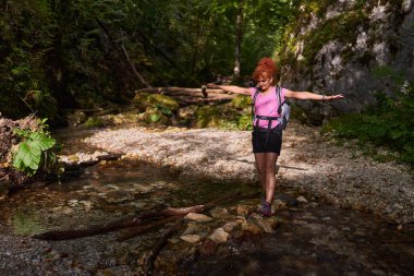 Yaz sonlarında dağlarda nehri geçen bir kadın yürüyüşçü.