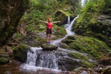Yazın sonlarında dağlarda şelalesi olan nehir kenarında yürüyüş yapan bir kadın.