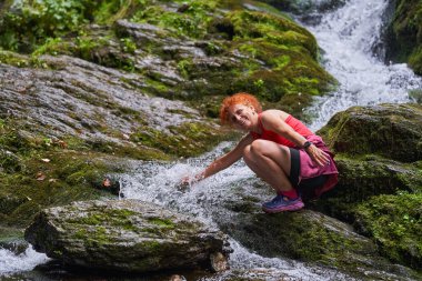 Yazın sonlarında dağlarda şelalesi olan nehir kenarında yürüyüş yapan bir kadın.