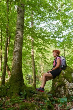 Sırt çantalı bir kadın ormanda dağlarda geziyor.