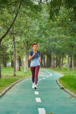 Kızıl saçlı kadın sabah parkta koşuyor.