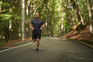 Yazın sonlarında sabah parkında koşan olgun bir adam.