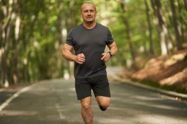 Atletik adam yazın sonlarında sabah parkta koşar.