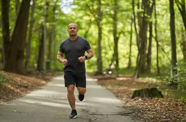 Sabahları güz parkında koşan atletik bir adamın gündüz görüşü 