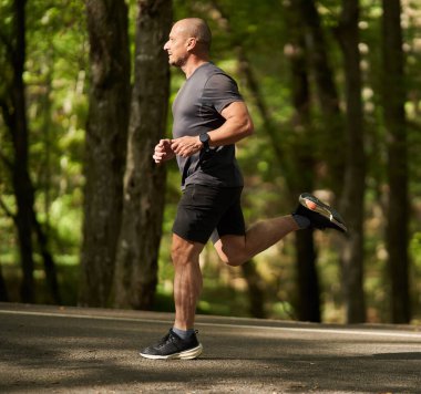 Atletik adam yazın sonlarında sabah parkta koşar.