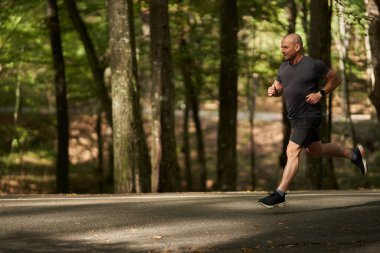 Atletik adam yazın sonlarında sabah parkta koşar.
