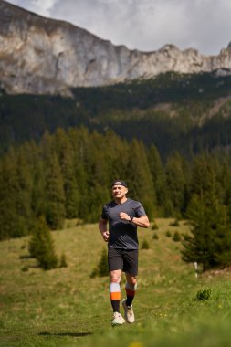 Patika koşucusu yüksek dağların aşağısındaki çayırda koşuyor.