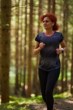 Yoğun bir çam ormanında koşan bir kadın koşucu.