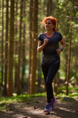 Yoğun bir çam ormanında koşan bir kadın koşucu.