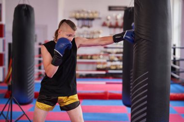 Genç kickboksçular kickboks salonunda kum torbasıyla antrenman yapıyor.