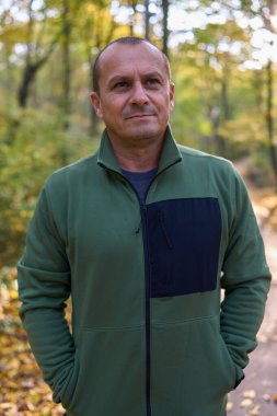 Çevresinde renkli sonbahar yaprakları olan orta yaşlı bir adam parkta. 