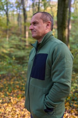 Orta yaşlı bir adam her yerde renkli sonbahar yapraklarıyla parkta yürüyüş yapıyor.