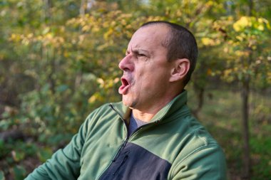 Mature man displaying various expressions during walk in autumn forest  clipart