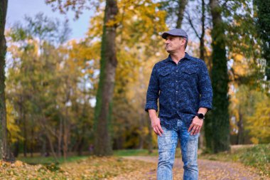 Renkli sonbahar yapraklarıyla parkta yürüyen bir adam. 