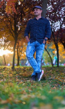 Orta yaşlı bir adam her yerde renkli sonbahar yapraklarıyla parkta yürüyüş yapıyor.