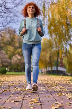 Sonbahar parkında sırt çantalı kıvırcık kadın. 