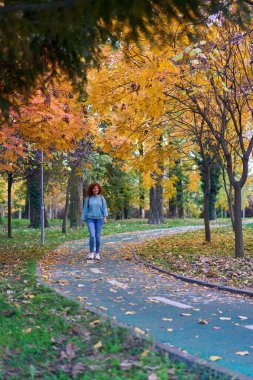 Parkta renkli bir sonbahar ortamında sırt çantalı kızıl saçlı kadın.