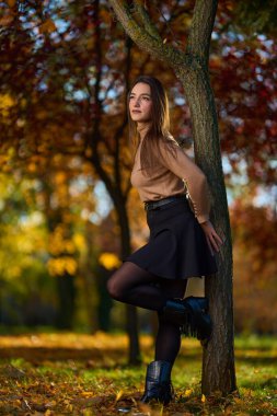 Sonbahar parkında ağaçlar ve yapraklarla çevrili İspanyol bir kadın.