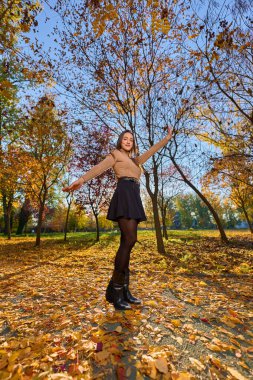 Parkta renkli ağaçlar ve sıcak bir günde yapraklarla dolu İspanyol genç bir kadın.