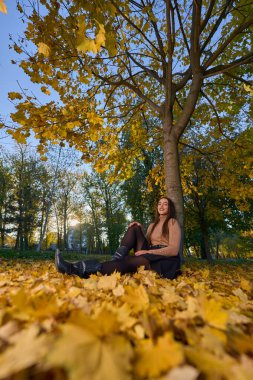 Güzel İspanyol kadın, renkli yapraklarla çevrili parkta oturuyor. 