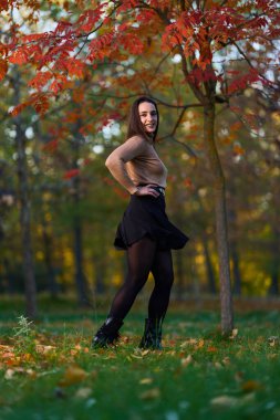 Parkta gülümseyen İspanyol kadın sonbahar günü etrafı renkli ağaçlarla çevrili.