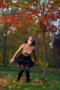 İspanyol genç kadın sonbahar parkında etrafı renkli ağaçlarla çevrili. 