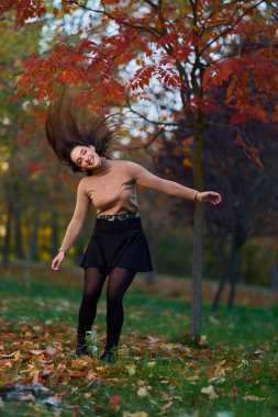 İspanyol genç kadın sonbahar parkında etrafı renkli ağaçlarla çevrili. 