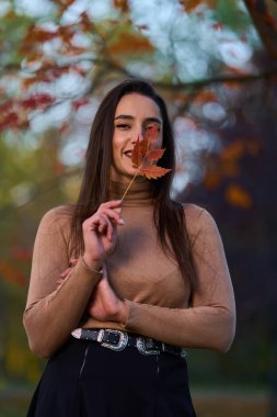 Parkta ağaçlarla çevrili renkli yapraklar tutan İspanyol genç kadının portresi. 