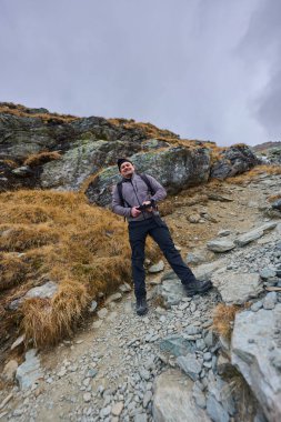 Sıcak giysili bir adam kayalık dağlarda patikada duruyor. 