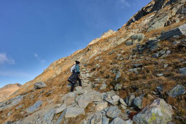 Sonbahar günü kayalık dağlarda engebeli patikada kadın yürüyüşçü.