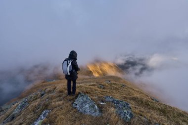 Soğuk bir sonbahar gününde, kayalık dağlarda, kalın giysiler ve kameralı yürüyüş yapan bir kadın.