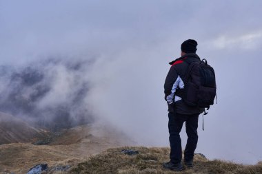 Sıcak giysili bir adam kayalık dağlarda patikada duruyor. 